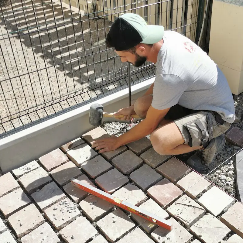 Technicien Fred Toma Rennes posant avec précision des pavés de grès avec maillet et niveau.