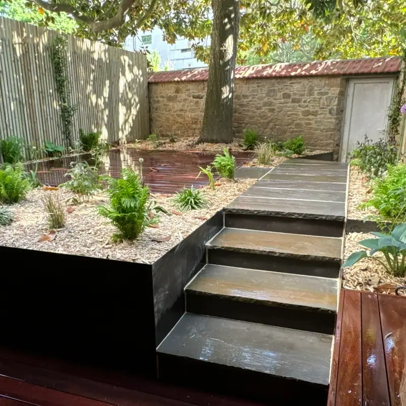 Aménagement paysager harmonieux combinant terrasse bois, dallage minéral et plantations à Rennes.